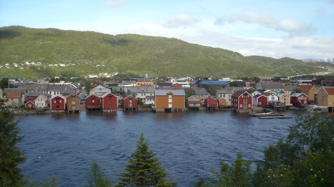Sjøgata i Mosjøen med de gamle trehusene langs Vefsna en sommerdag, med grønn ås i bakgrunnen