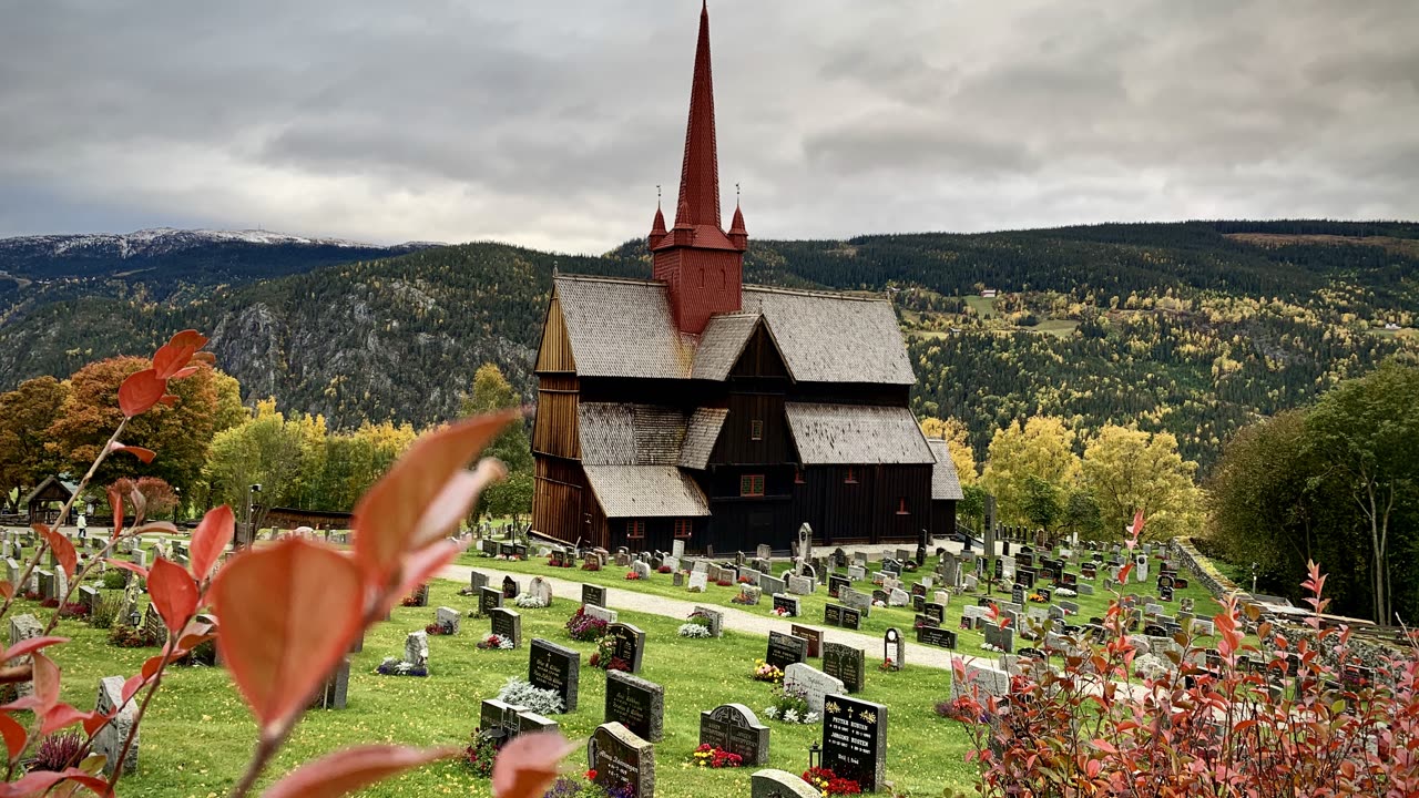 Ringebu stavkirke fra 1200-tallet med rød tårnhjelm i Gudbrandsdalen, med skogkledde dalsider bak