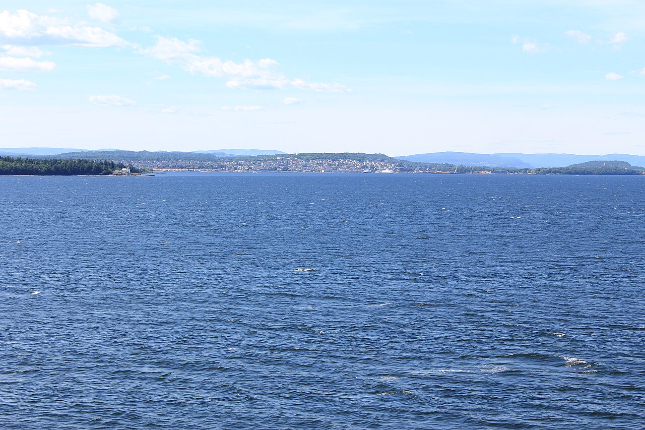 Sandefjord sentrum sett fra fjorden en sommerdag, med byens bebyggelse og havnepromenade langs vannkanten
