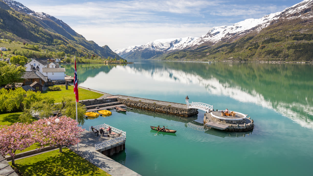 Sørfjorden ved Lofthus i Hardanger med snøkledde fjell, frukttrær i blomst og en brygge ut i fjorden