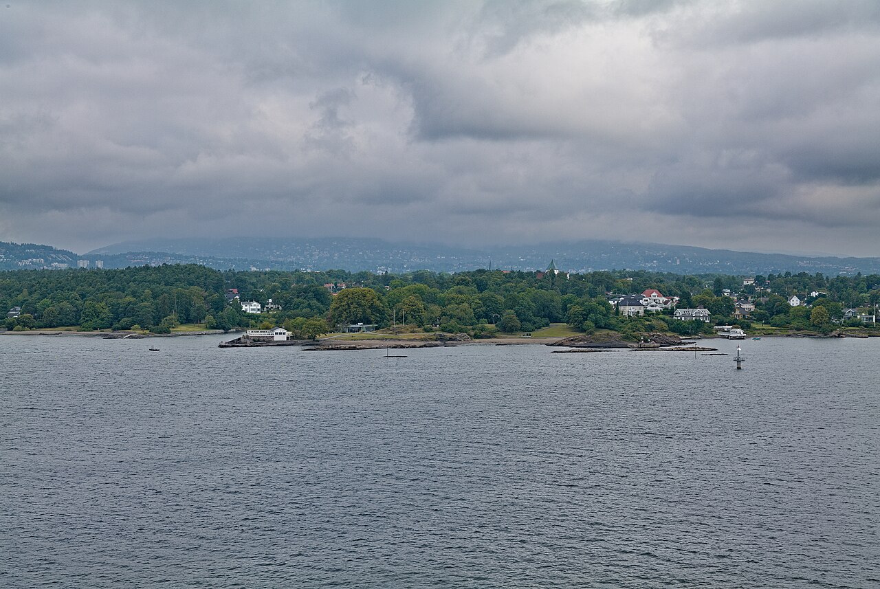 Nesodden-halvøya sett fra en ferge på Oslofjorden en sommerdag i august, med skogskledd kystlinje og blå himmel
