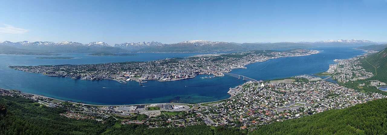 Panoramautsikt over Tromsøya fra Fjellheisen med Ishavskatedralen og Tromsø bru i forgrunnen, bysentrum og havna i midten, og fjell og øyer i bakgrunnen